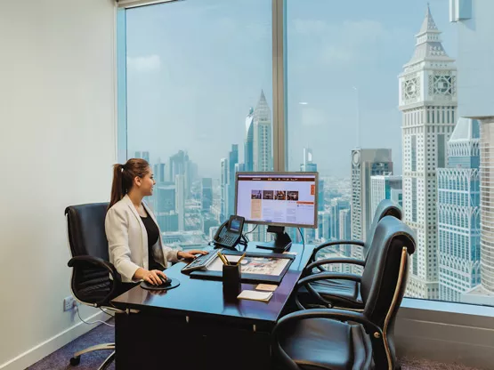 A professional woman working at her desk in a modern Servcorp private office, with a stunning panoramic view of Dubai’s skyline, at Almas Tower, Dubai